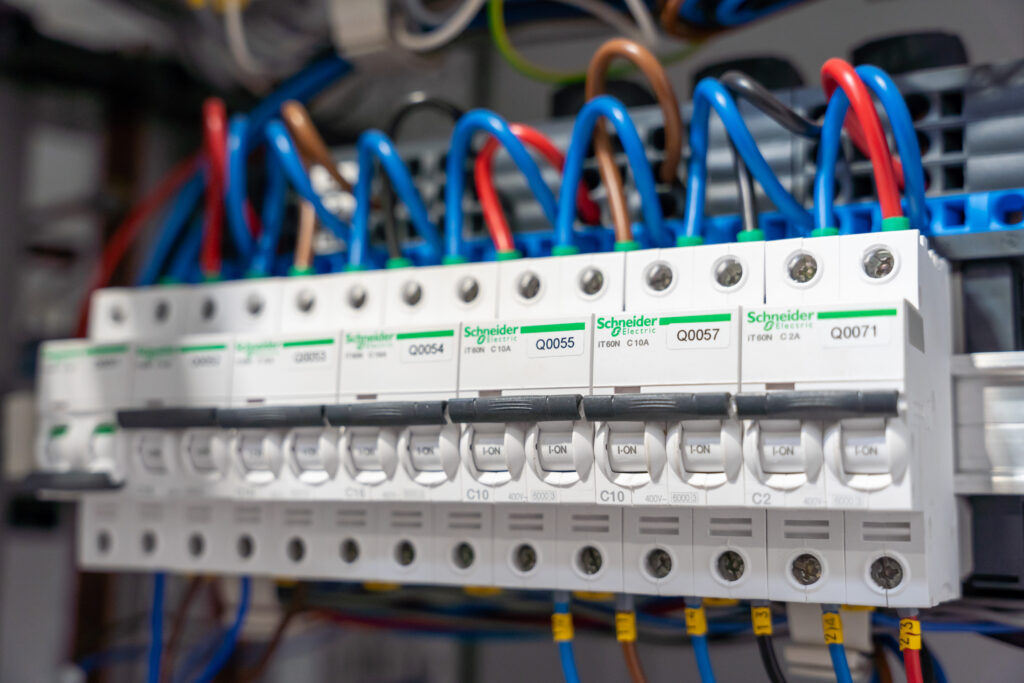 Disjoncteurs modulaires et câblage des circuits électriques de protection dans une armoire industrielle. Armoire électrique de commande à proximité d'une ligne de convoyage automatisée avec bande modulaire bleue à Rochefort.