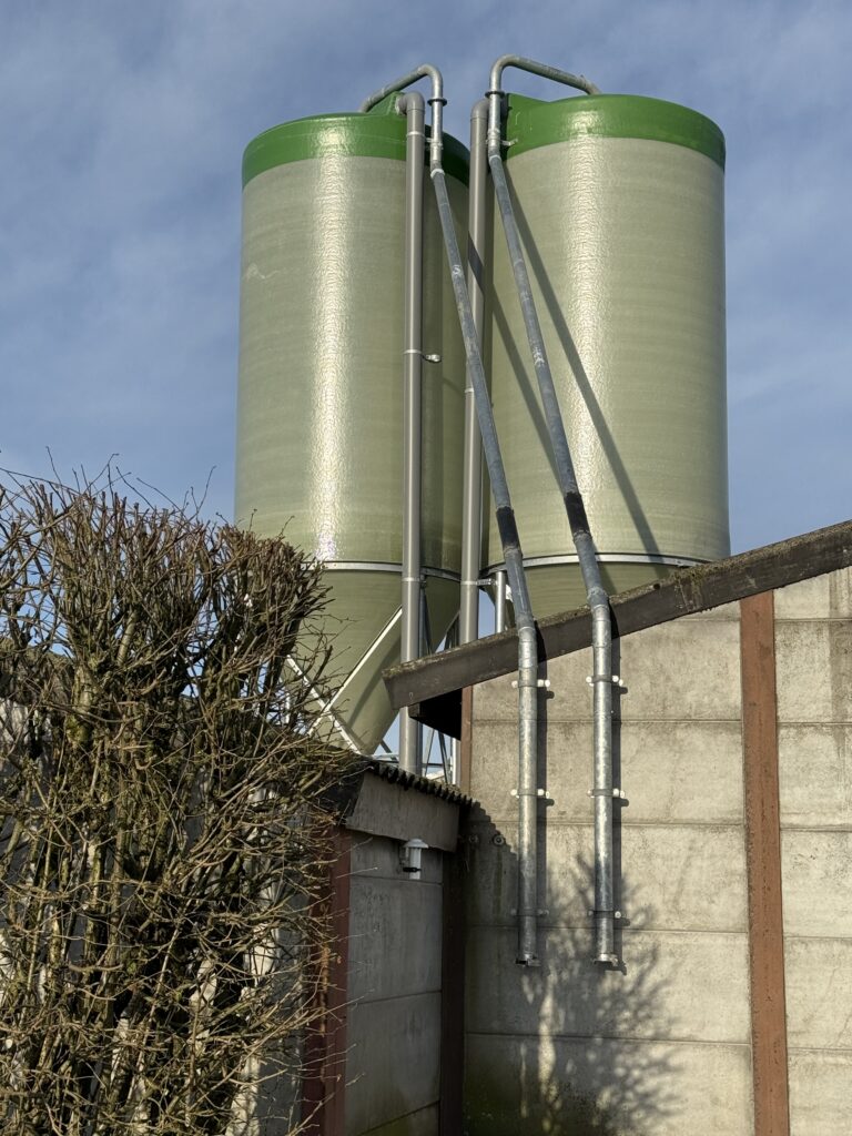 Silos d'aliments avec tuyauteries de transfert installés à l'extérieur d'un bâtiment avicole à Libramont.