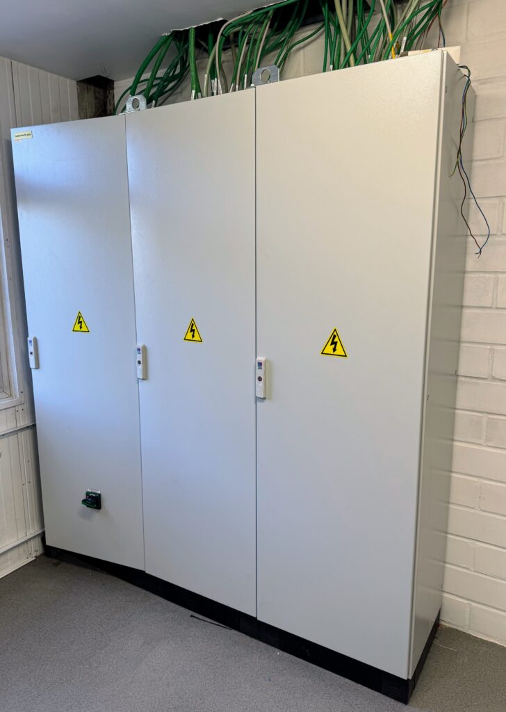 Armoires électriques métalliques de distribution avec signalisation de danger électrique dans un bâtiment industriel.