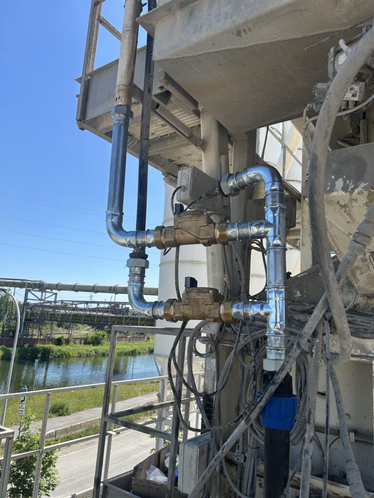 Vue des tuyauteries et des électrovannes du circuit de remplissage d'eau d'une centrale à béton à La Louvière.