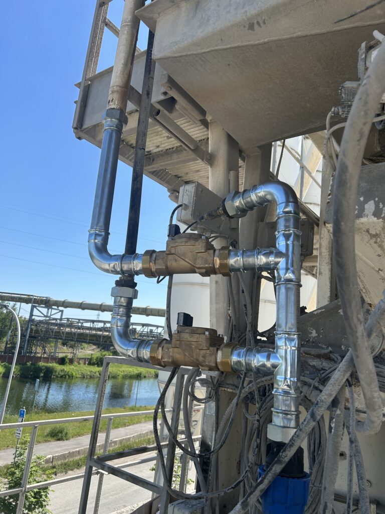 Circuit de remplissage d'eau d'une centrale à béton à La Louvière, avec tuyauteries métalliques et électrovannes.