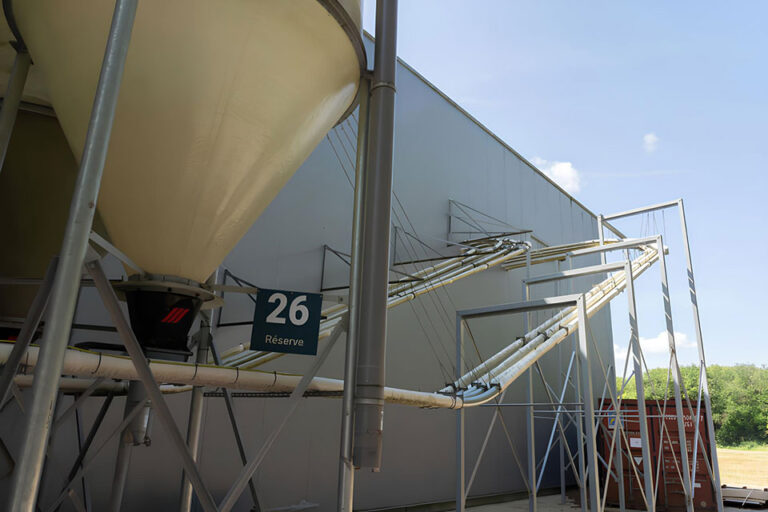 Silos industrielle extérieure raccordée à un système de convoyage sur structure métallique.